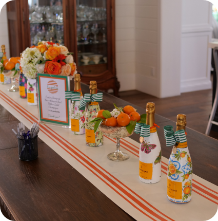Gallery - bottles lined up in the table with flowers and fruits.